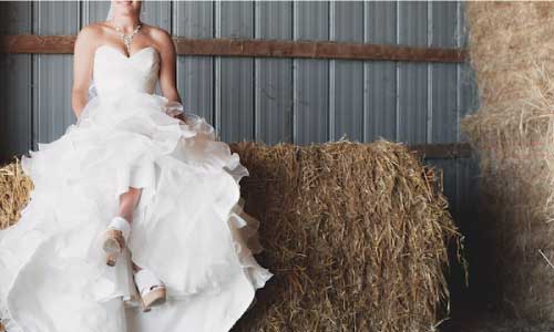 bride sitting on bale of hay with crossed ankles