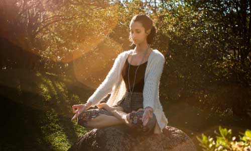 young pretty lady sitting on rock in Lotus Pose at sunrise
