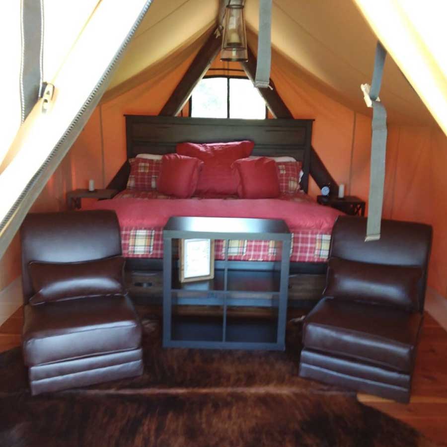Ben's Quarters glamping tent interior of king size bed, two comfy chairs, a bear skin rug, two nightstands and a small book shelf